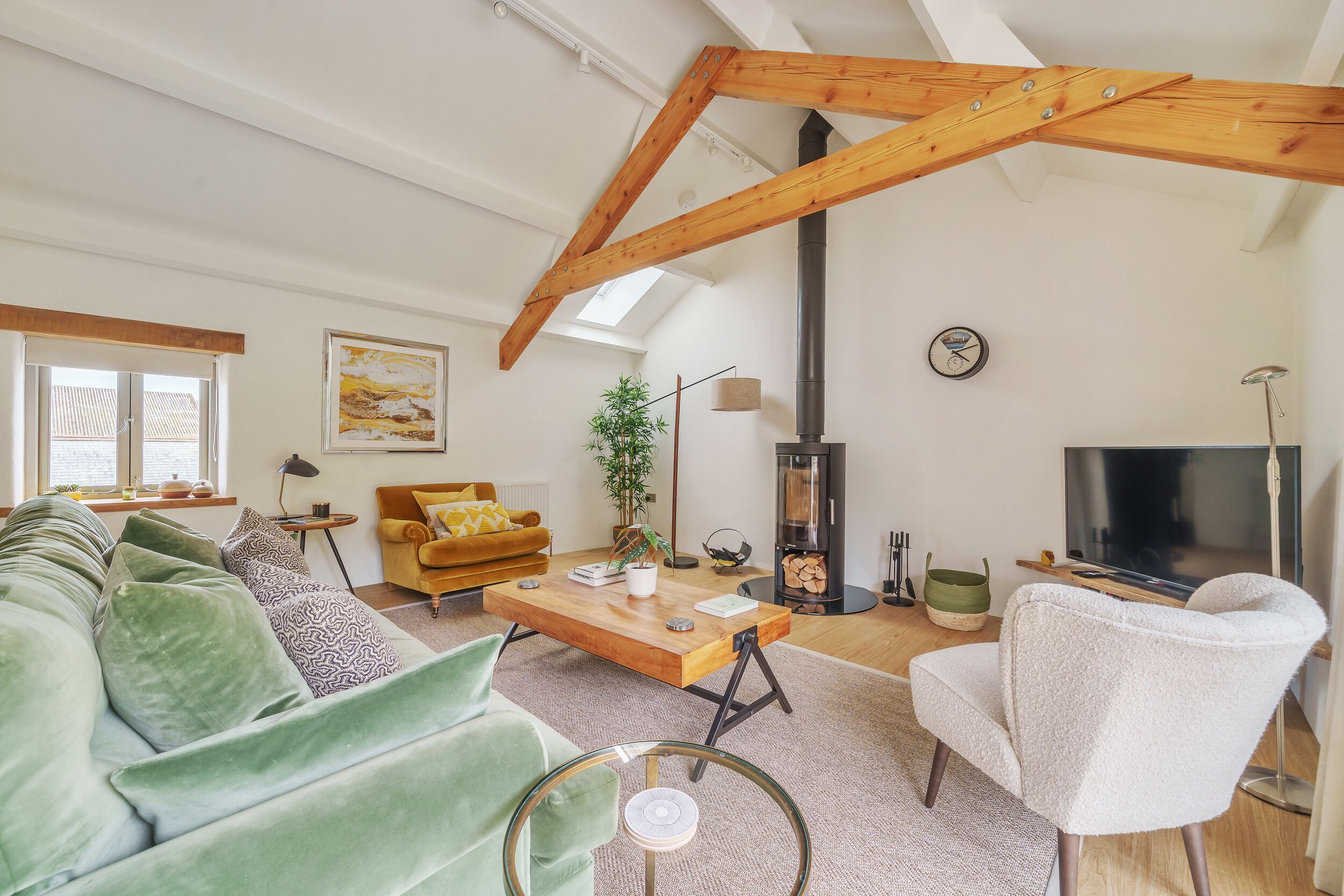 Una sala de estar moderna con techo de madera, un sofá verde, un sillón blanco, una mesa de centro y un televisor.