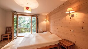 Ein Schlafzimmer mit einem hölzernen Bett, einer Bank, einem Nachttisch und Blick ins Freie durch eine Schiebetür.