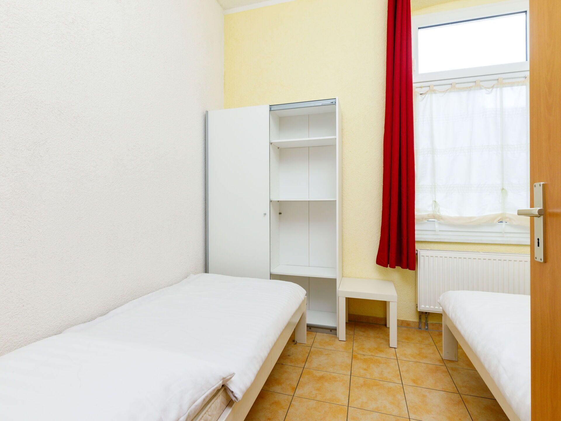 A small, tidy room with two single beds, a white wardrobe, and a small table.
