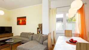 Una sala de estar con sofá, reposapiés, mesa de centro, televisor, estantería y mesa de comedor con sillas.