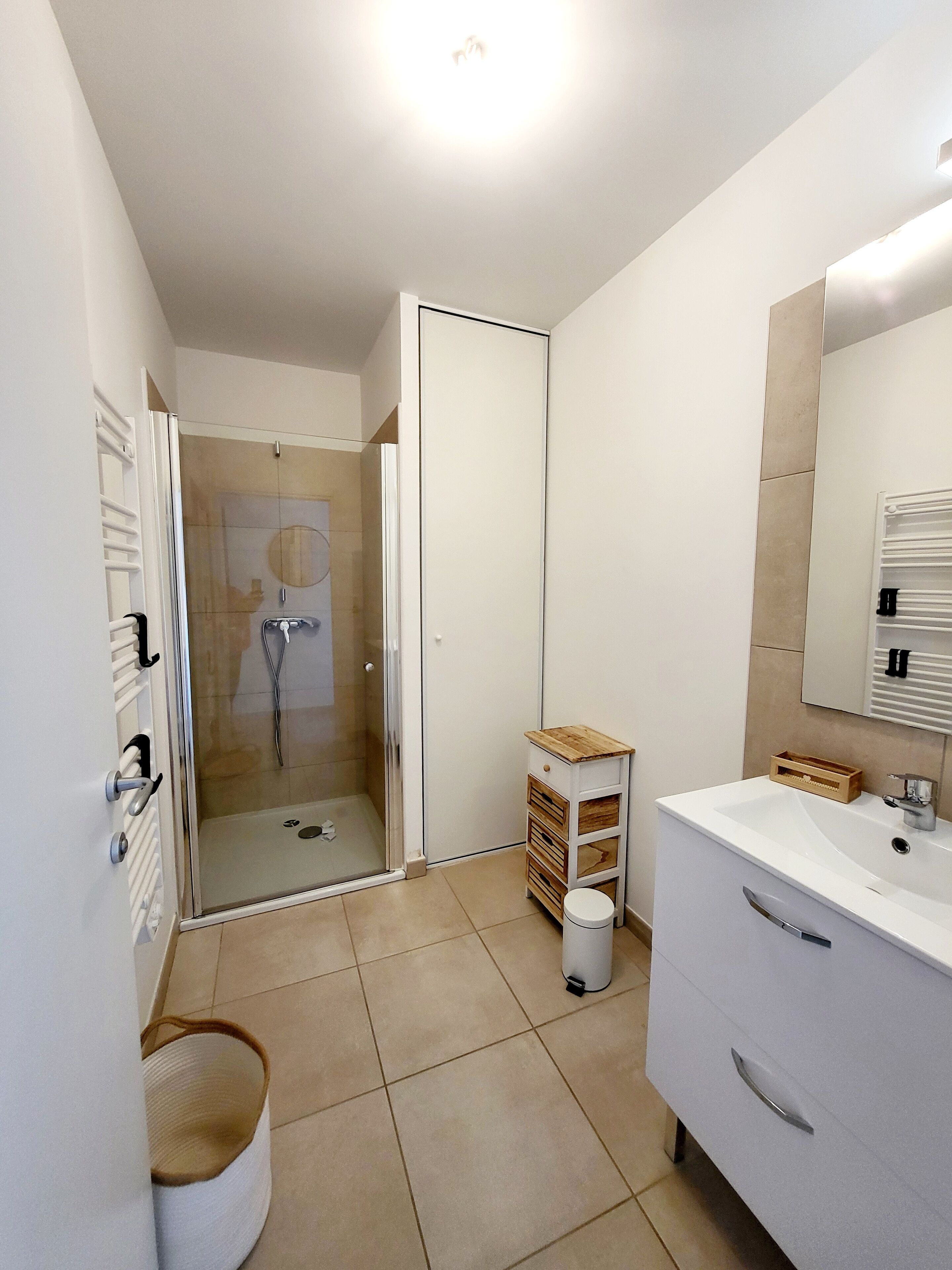 Une salle de bain moderne avec une douche à parois de verre, un meuble-lavabo blanc avec un miroir et un sol carrelé de couleur beige.