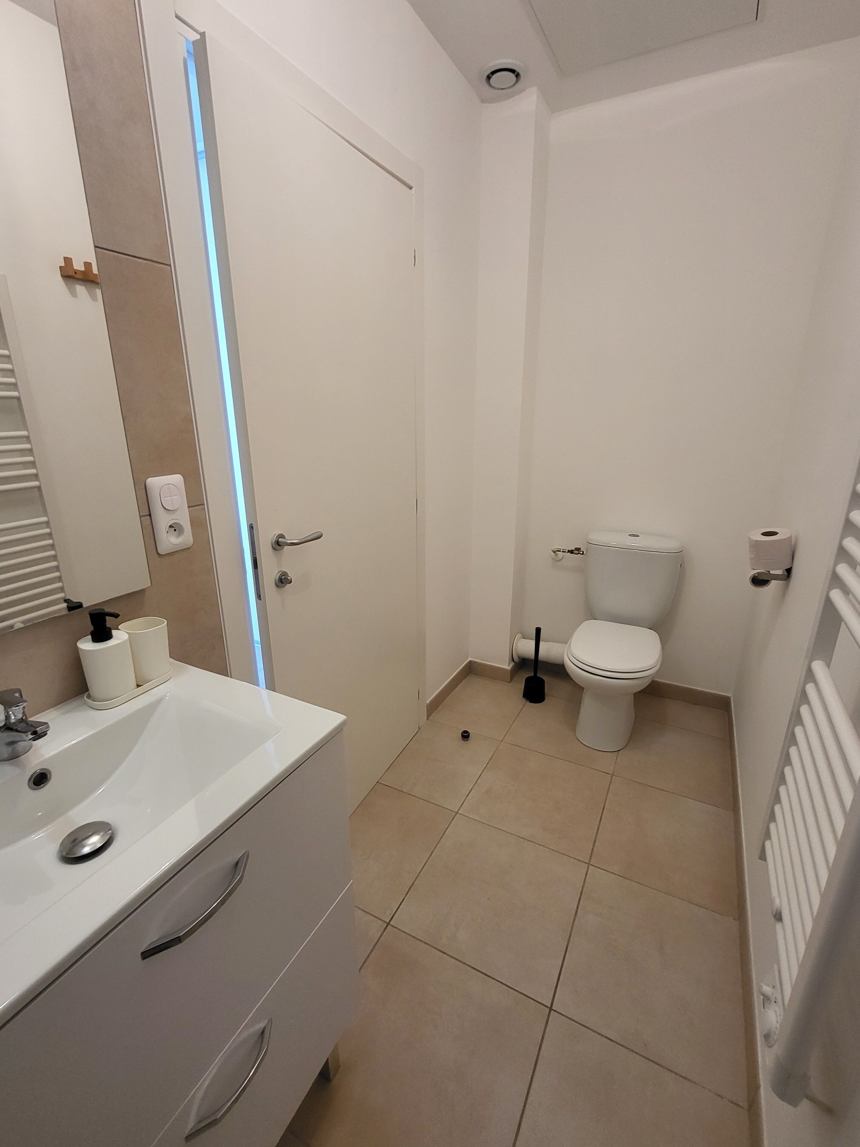 Moderni kylpyhuone, jossa on valkoinen pesuallas, peili ja wc-istuin.