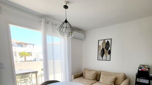 Un soggiorno con un tavolo rotondo, quattro sedie, un divano beige, un'opera d'arte appesa al muro e un condizionatore d'aria.