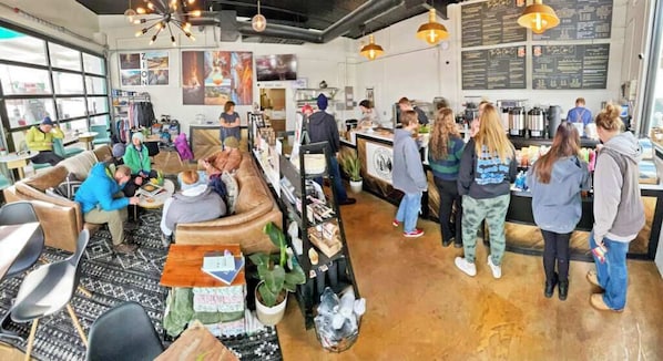 Un café doté d’un long comptoir, d’un espace salon et de grandes fenêtres.