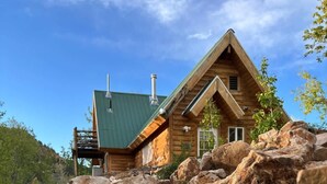 Eine Blockhütte mit einem grünen Dach, umgeben von großen Steinen und einem klaren Himmel.