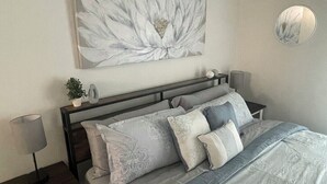 Un dormitorio con una cama, mesitas de noche, un espejo montado en la pared y una obra de arte floral grande.