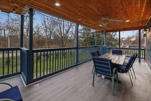 Une terrasse extérieure couverte, dotée d’un plafond en bois, d’une table avec des chaises et offrant une vue sur une courClose.