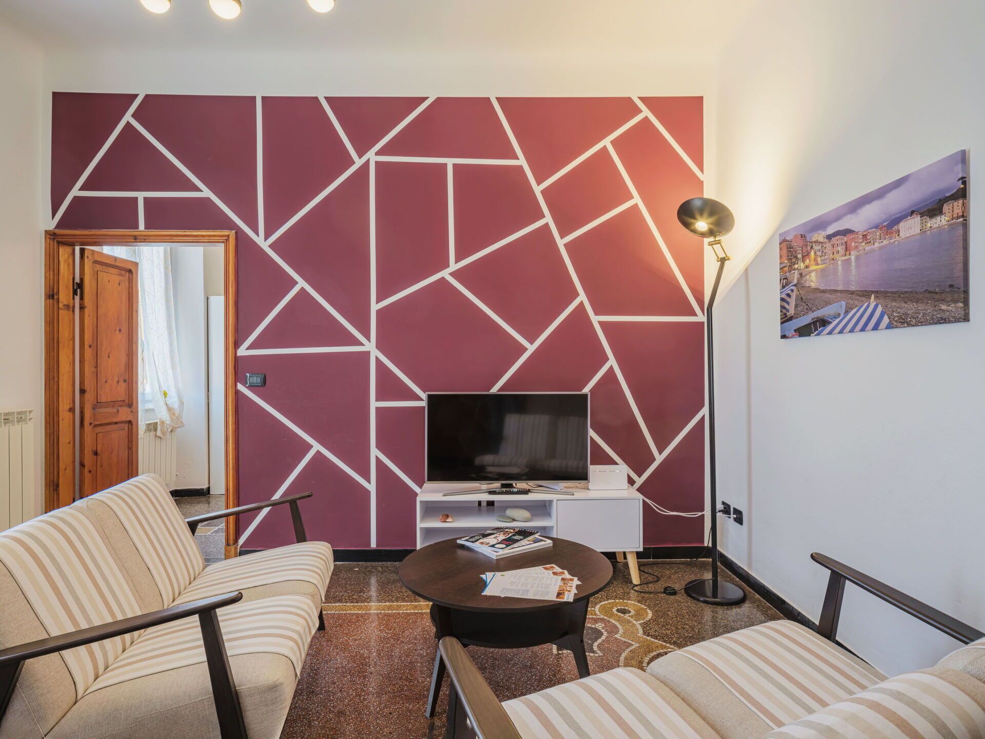 Una sala moderna con una pared de estampado geométrico, un televisor de pantalla plana, una mesita de centro y sofás a rayas.