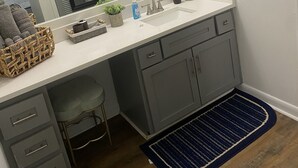 Une salle de bain moderne avec un grand miroir, des meubles gris, un lavabo blanc et un tapis bleu.