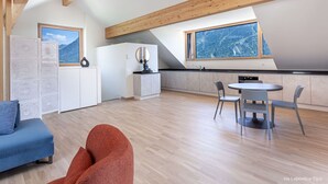 A modern kitchen with a large window, wooden beams, and a dining area with chairs.