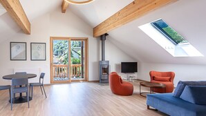 A spacious living area with a wooden ceiling, a large window, a fireplace, and a blue sofa.