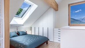 A bedroom with a skylight, a bed, a dresser, and a view of mountains.