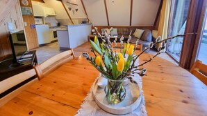 Een gezellig houten interieur met een eettafel, een vaas met bloemen en een keuken op de achtergrond.