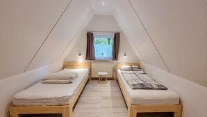 Een kleine zolderkamer met twee eenpersoonsbedden, een klein tafeltje en een raam met gordijnen.