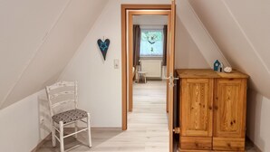 Een kleine zolderkamer met een houten kast, een witte stoel en een hartvormige decoratie aan de muur.