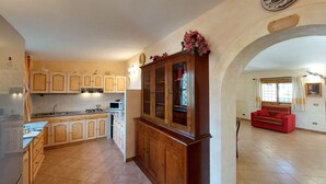 Cozinha ampla com armários de madeira e uma ilha central, área de jantar com sofá vermelho e um arco decorativo.