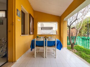 A small patio area with a table and chairs, a window overlooking a balcony, and a green fence in the background. - Beautiful apartment for 4 guests with pool, A/C, WIFI, TV and panoramic view (Villasimius)
