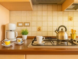 A kitchen with a gas stove, coffee maker, tea kettle, and various cups and saucers on the counter. - Lovely apartment for 4 guests with WIFI, A/C, TV and balcony (Villasimius)