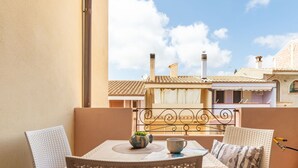 Un balcon avec des fauteuils en osier et une table, une vue sur les immeubles et un ciel dégagé.