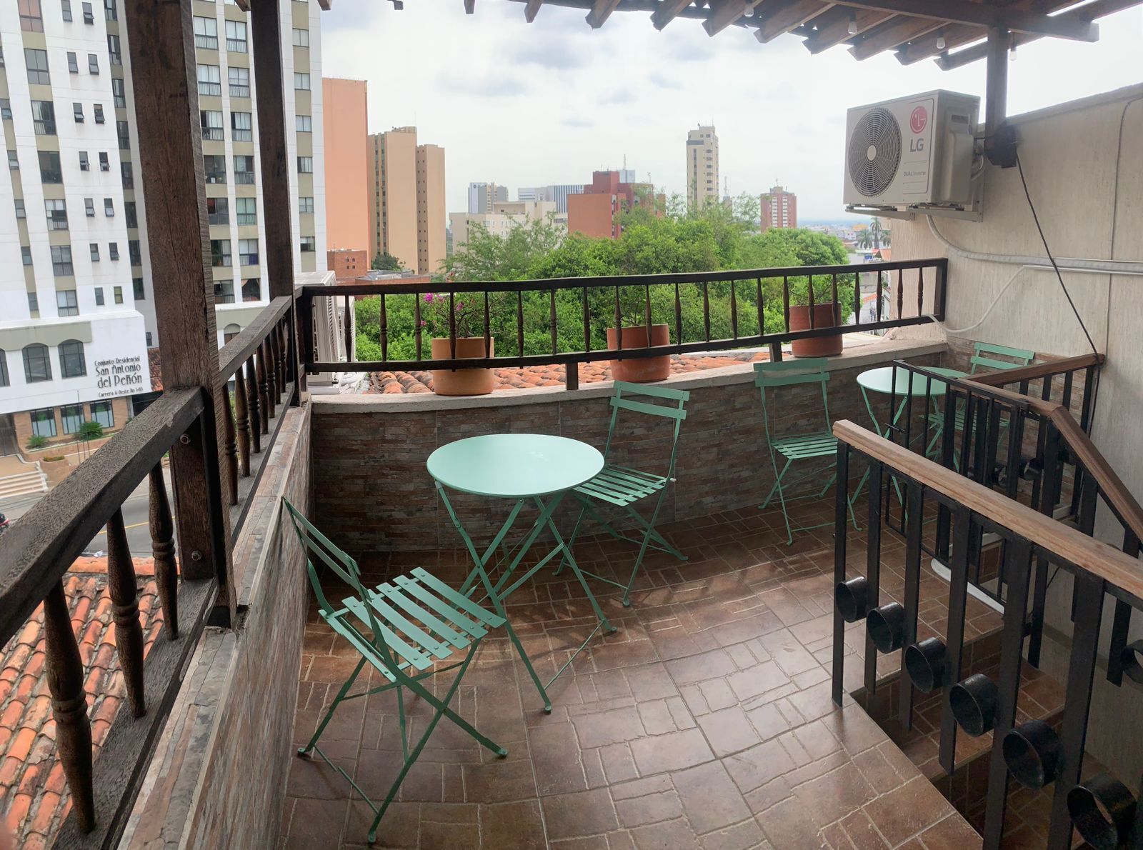 Ein Balkon mit grünen Metallstühlen und einem runden Tisch, einem Blumentopf und Blick auf Stadtgebäude.