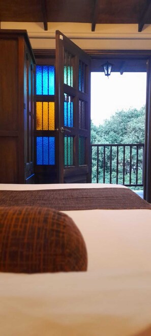A room with a bed, a wooden door with stained glass, and a balcony with a railing. - HOTEL ALTANA (Cali)