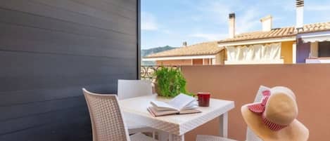 A balcony with a table, chairs, a book, a red mug, and a straw hat.