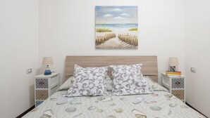Un dormitorio con cama, dos mesitas de noche, una mesilla auxiliar, un cuadro en la pared y una colcha estampada.