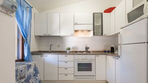 Una cocina compacta con armarios blancos, estufa a gas, horno empotrado y refrigerador.