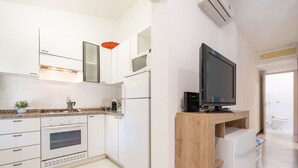 Una cocina moderna con armarios blancos, horno empotrado, refrigerador y un mueble de televisión de madera.