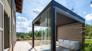 Un espace extérieur moderne, aménagé avec une structure vitrée, une terrasse en bois et offrant une vue sur le paysage environnant.