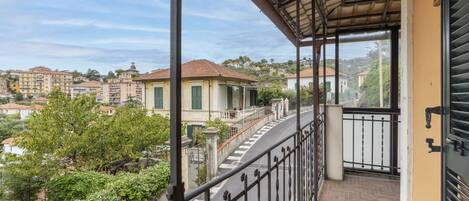 A balcony with a metal railing overlooking a residential area with houses and greenery.