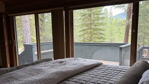 Un dormitorio con una cama grande, una ventana y vistas a árboles y una terraza exterior.