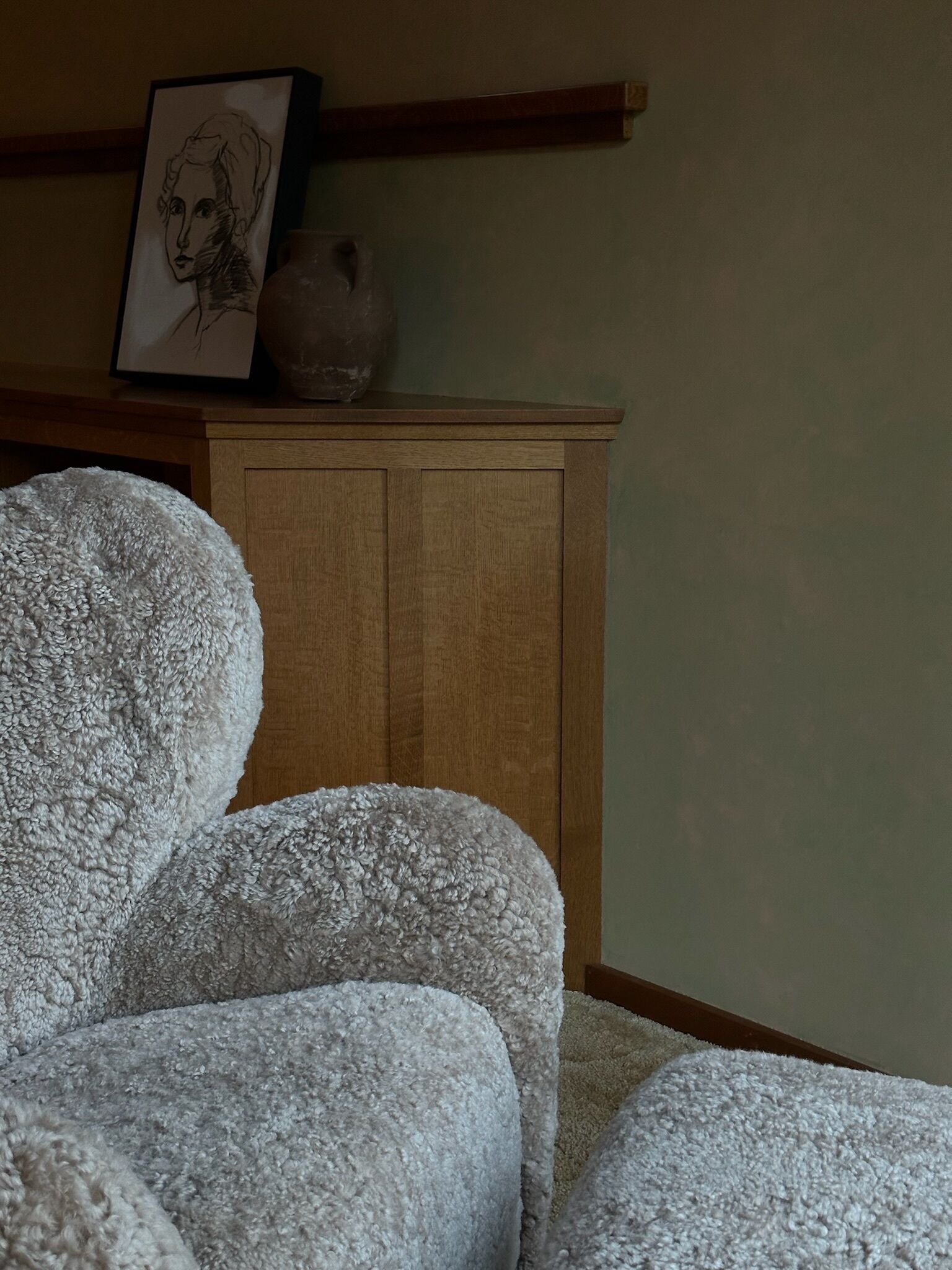 A room with a large, fluffy white chair, a wooden cabinet, and a framed picture on the wall.