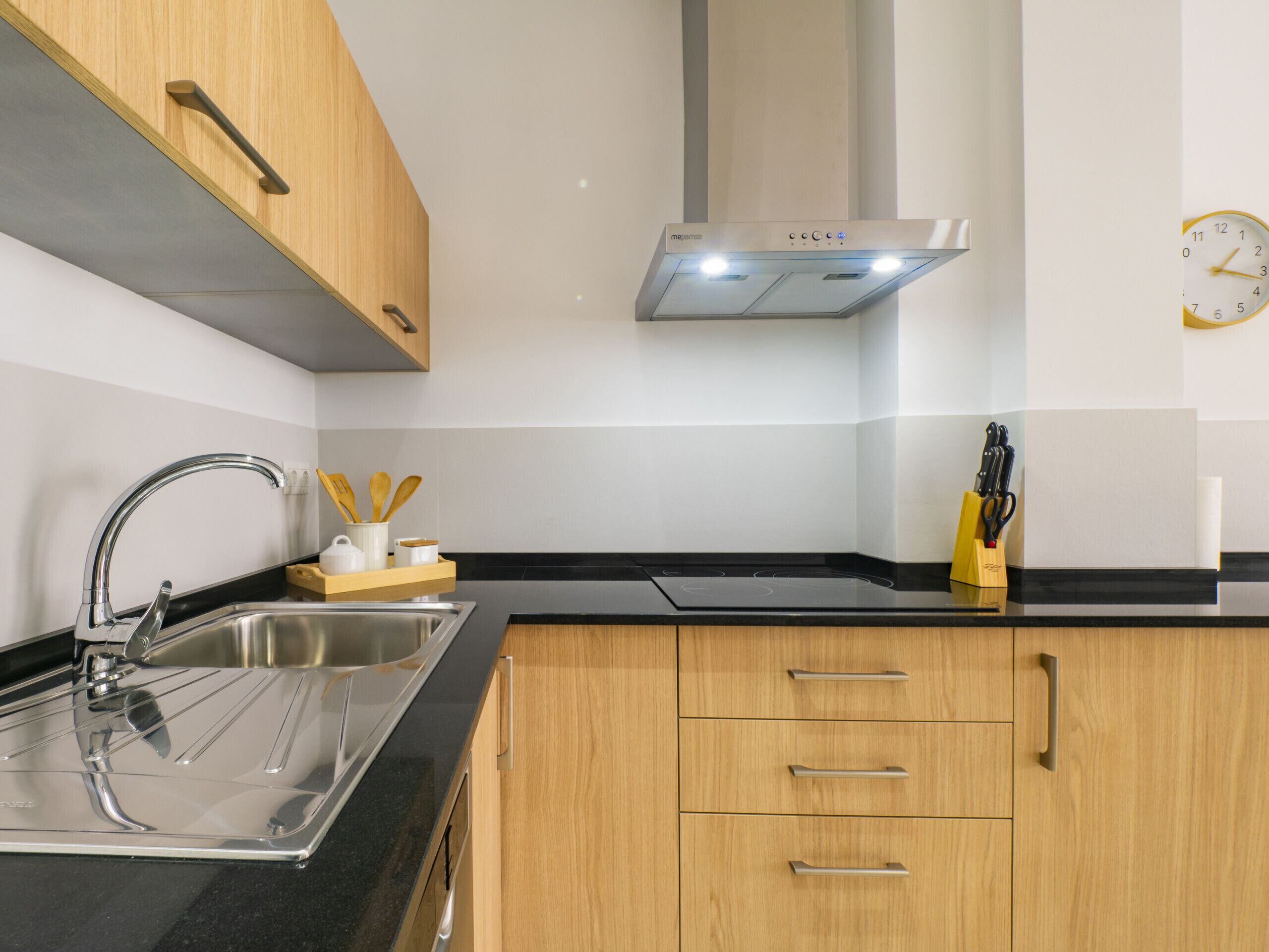 Een moderne keuken met een roestvrijstalen spoelbak, houten kastjes en een zwart aanrecht.