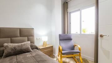 Une chambre à coucher avec un lit, une table de chevet, une lampe, une chaise et une fenêtre.