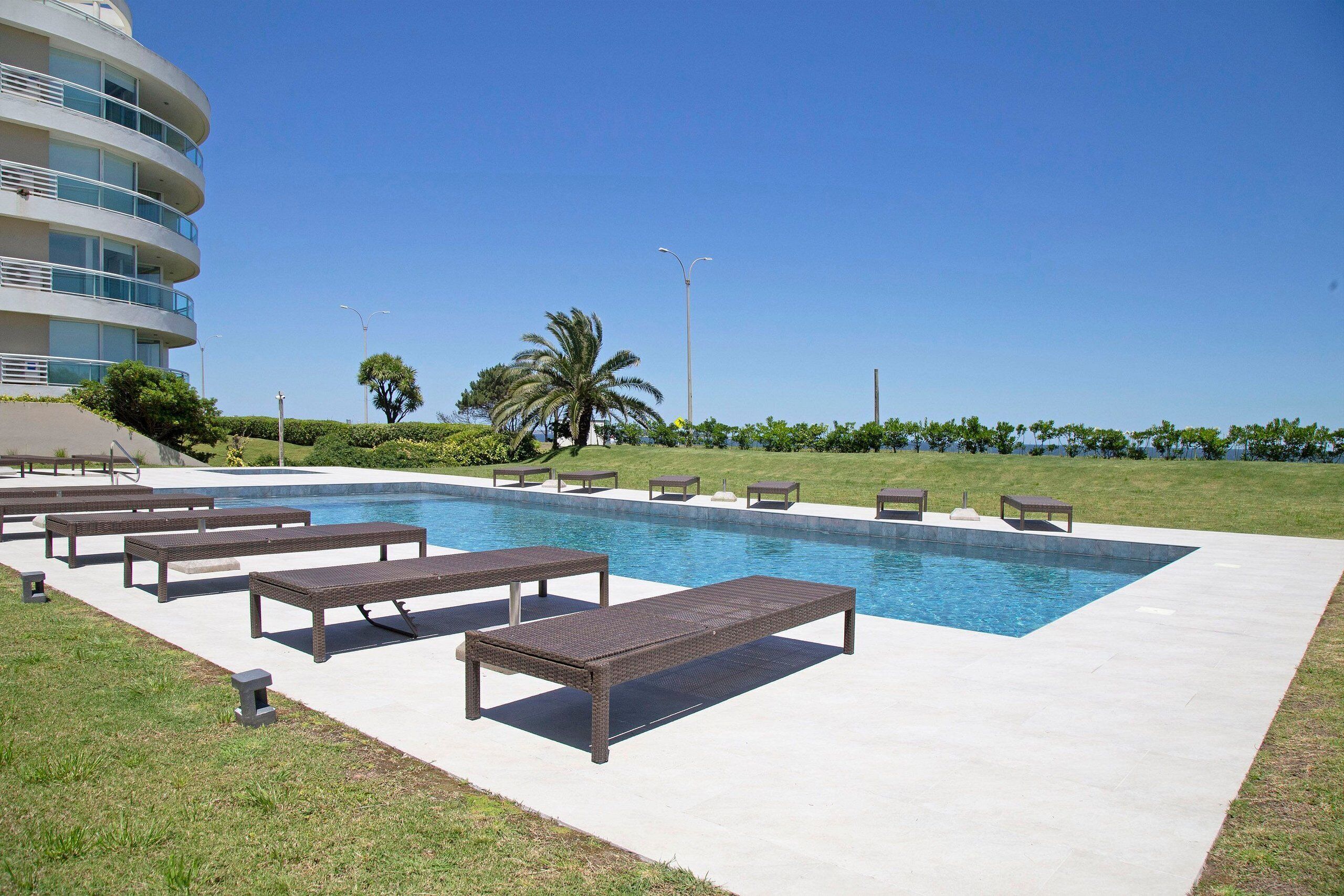 A swimming pool with lounge chairs and a building in the background.