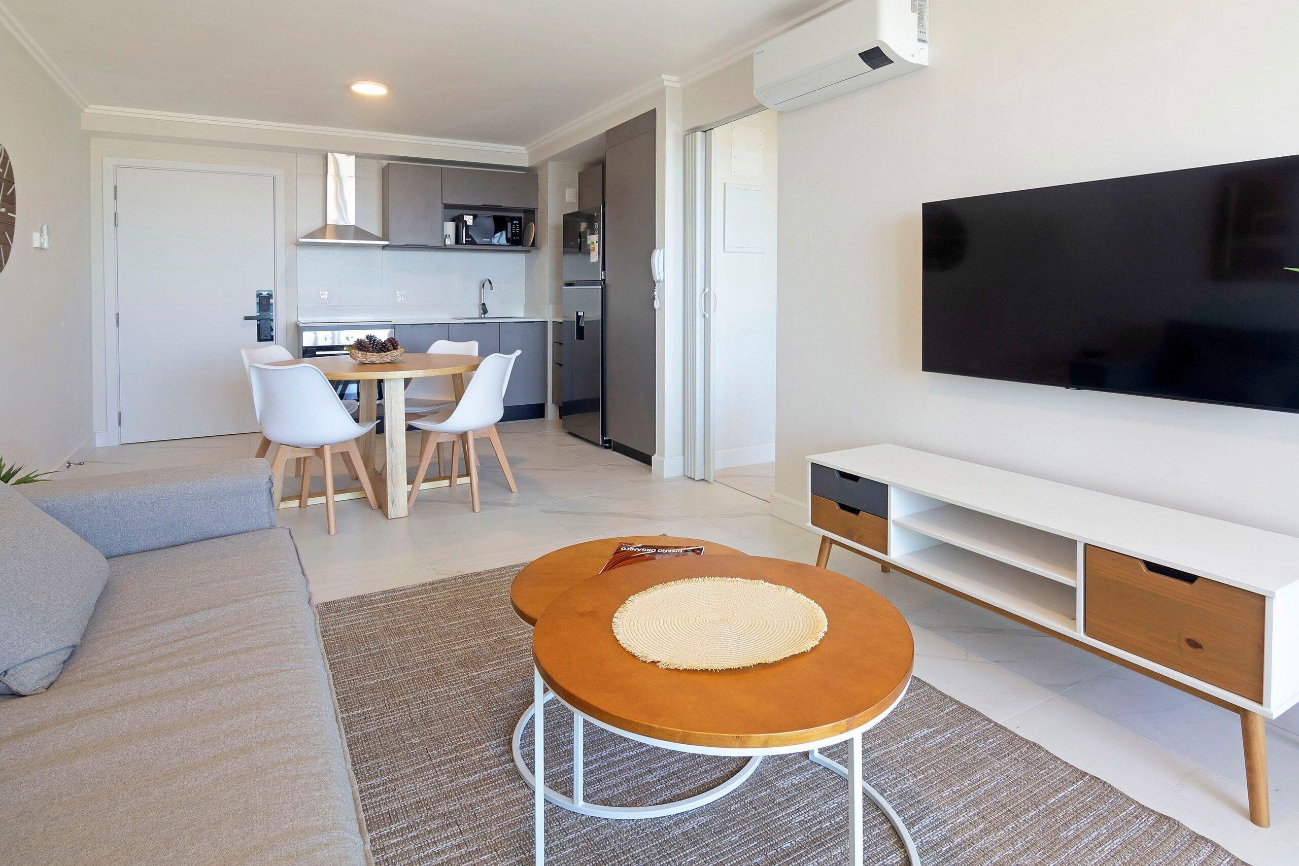 A modern living room with a sofa, a coffee table, a TV, a kitchen area, and a dining table.