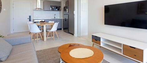 A modern living room with a sofa, a coffee table, a TV, a kitchen area, and a dining table.
