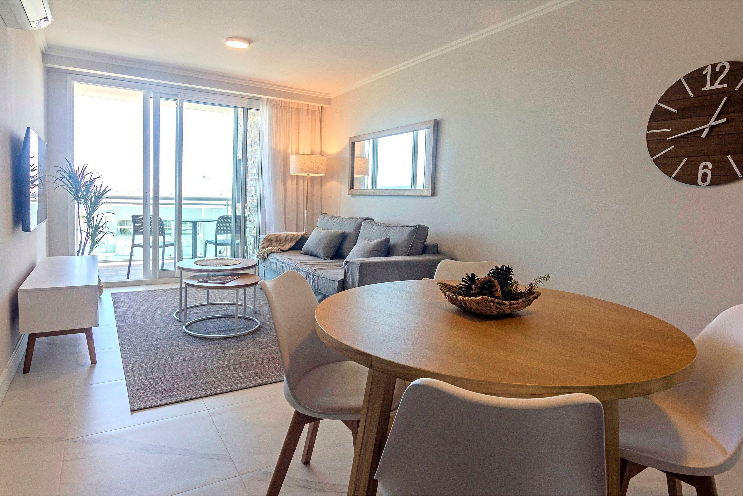 A modern living room with a sofa, a dining table, and a large wall clock.