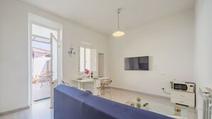 A modern living room with a blue sofa, a dining area with a table and chairs, a TV mounted on the wall, and a kitchen area with a microwave. - Beautiful private villa for 8 people with A/C, TV and patio (Viareggio)