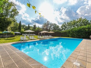 A rectangular swimming pool with clear blue water, surrounded by a tiled deck. There are lounge chairs and umbrellas arranged around the pool, and a stone wall in the background. - Cosy apartment for 29 guests with private pool, WIFI, TV, patio, pets allowed and panoramic view (Pergine Valdarno)