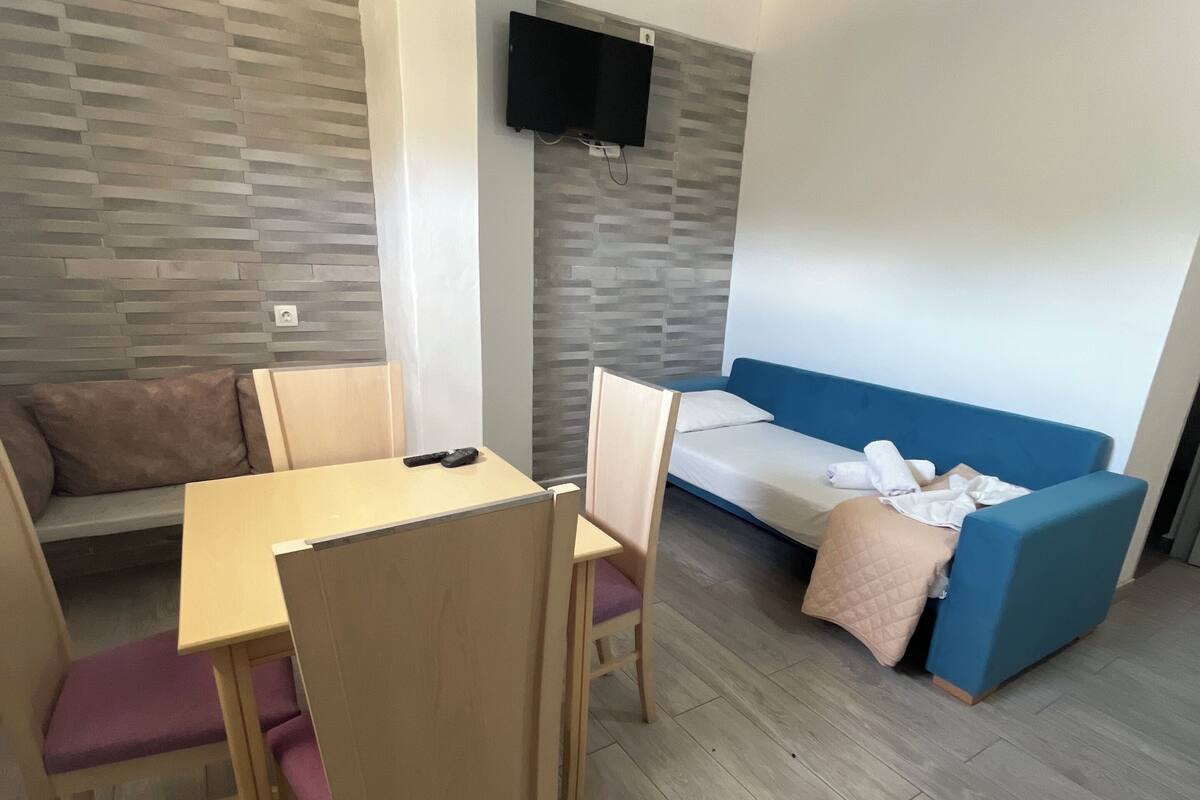 A modern room with a dining table, chairs, a sofa, and a TV mounted on the wall.
