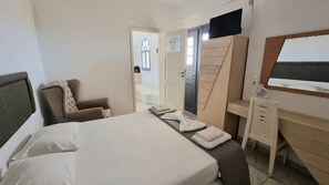 A hotel room with a bed, a chair, a desk, and a wardrobe. - Leon Lux Apartments (Santorini)