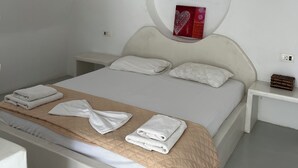 Un dormitorio con cama, paredes blancas, un elemento decorativo circular en el techo, una mesita de noche y una lámpara colgante.