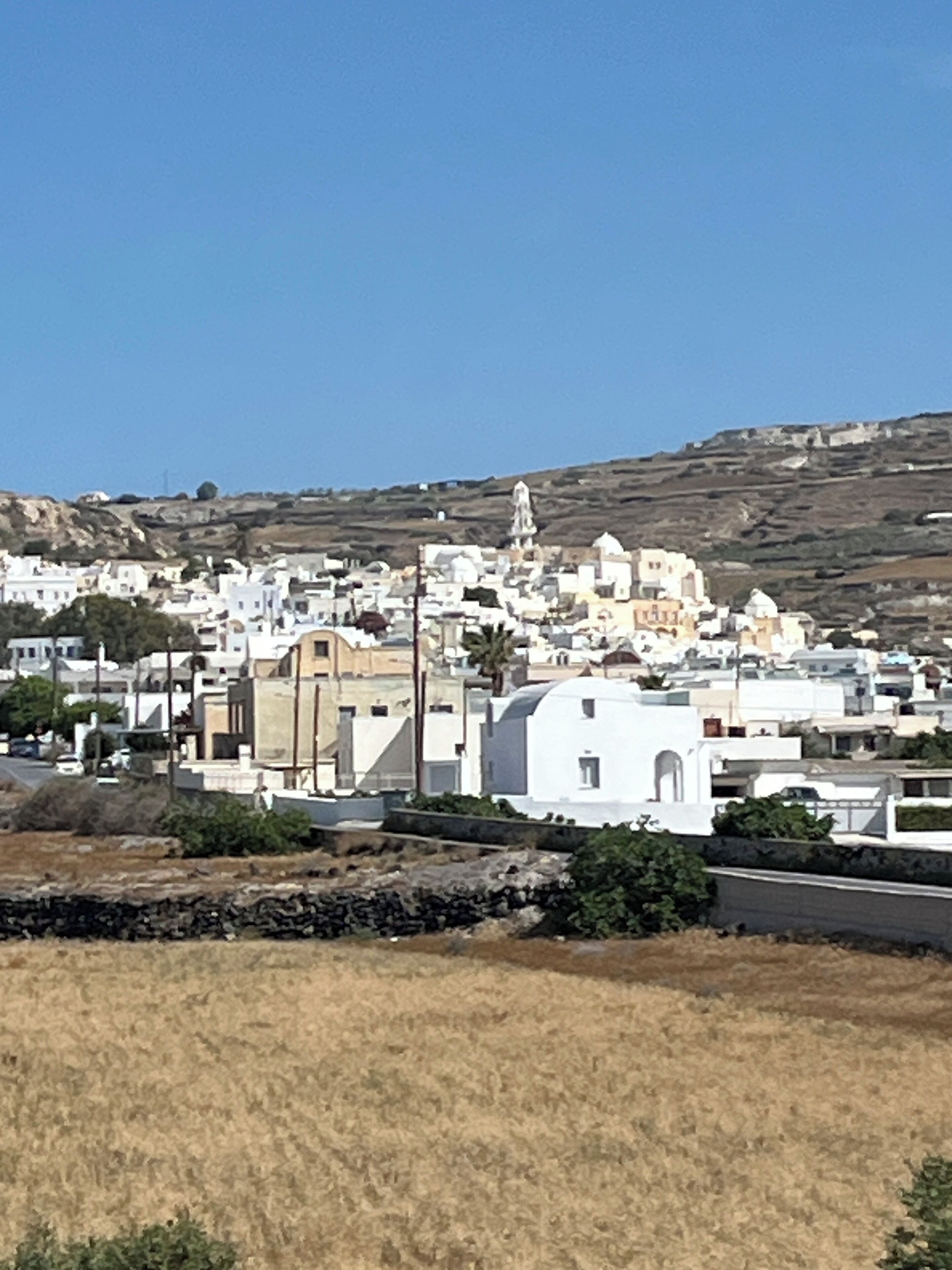A coastal town with white buildings, a prominent church, and a hillside in the background.