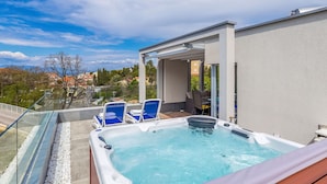Ein Poolbereich auf dem Dach mit Whirlpool, Liegestühlen und einer Glasbrüstung mit Blick auf die Stadt.