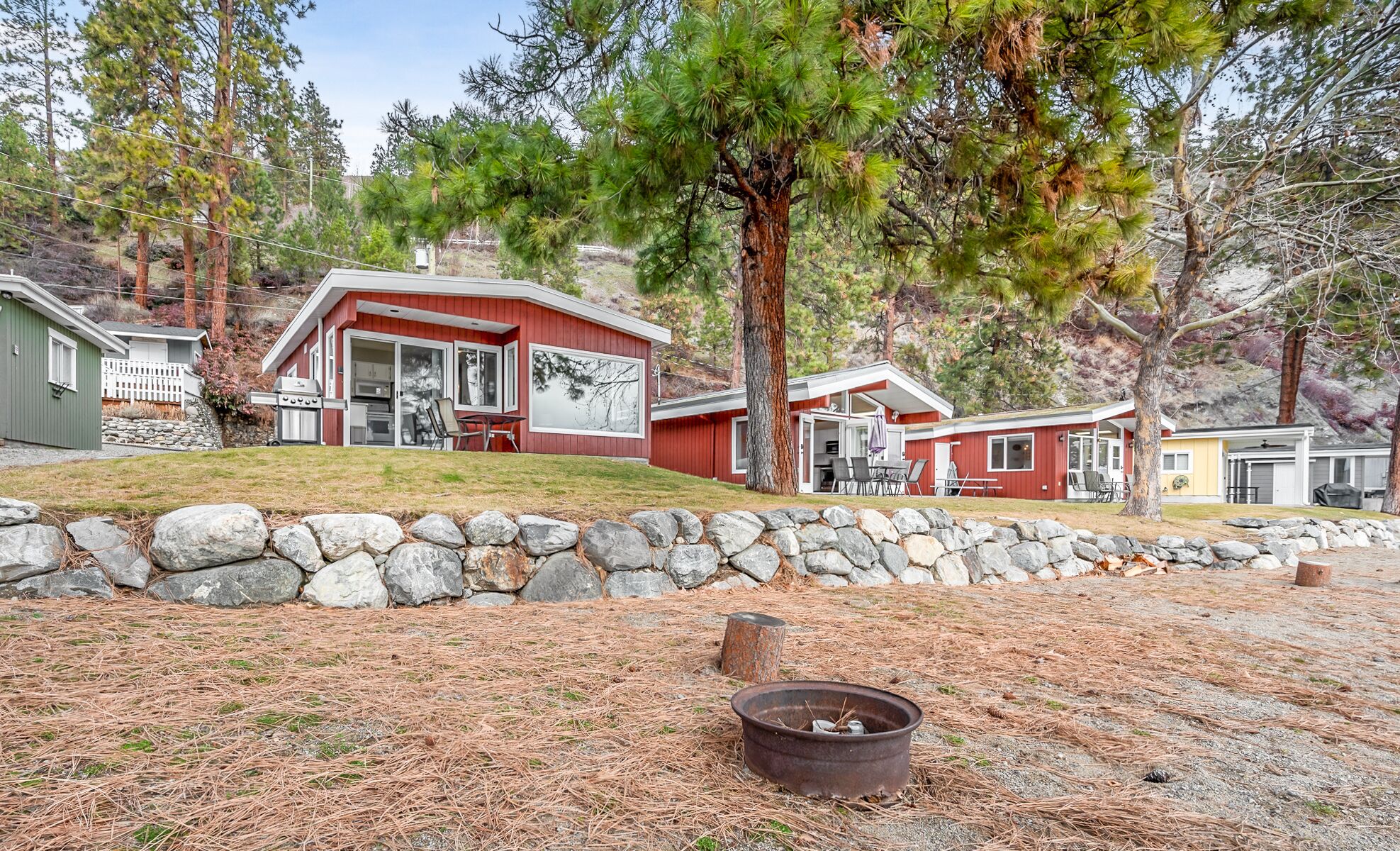 A red cabin with a stone wall and a fire pit in the foreground.