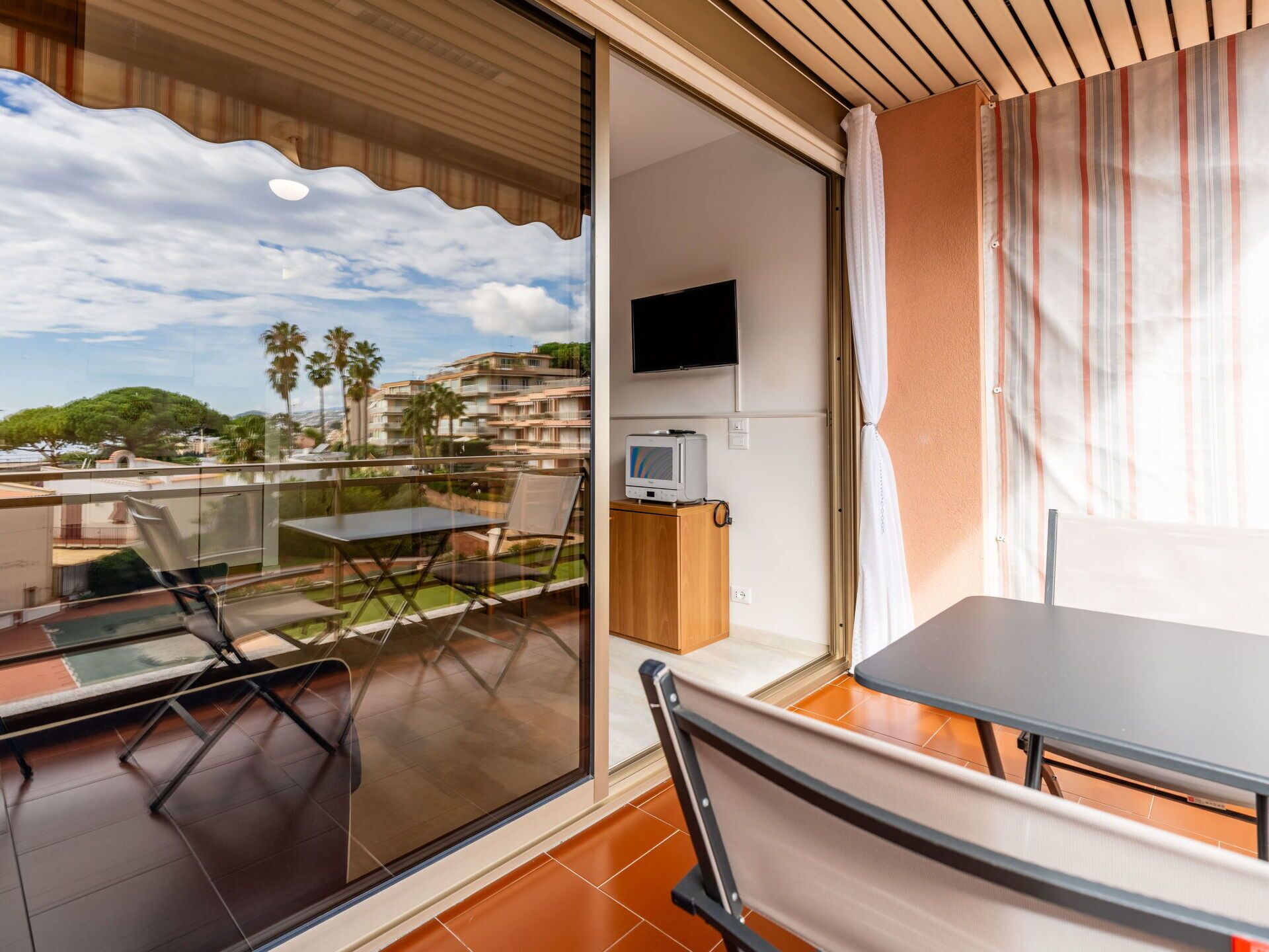 A balcony with a table and chairs, a TV, and a view of buildings and palm trees.