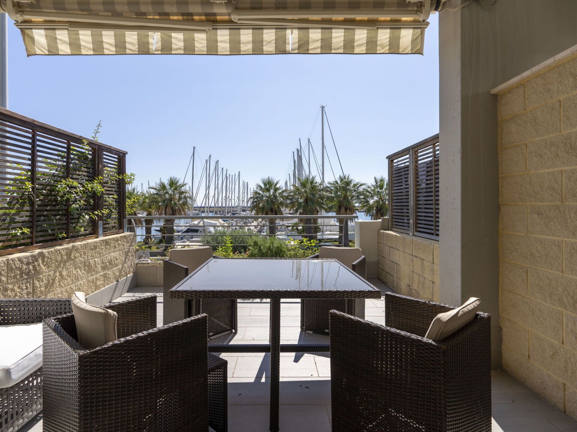 Eine Terrassenanlage im Freien mit Tisch und Stühlen, mit Blick auf einen Jachthafen und Boote.