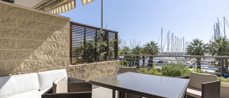A terrace with wicker furniture, a white sofa, and a view of a marina with boats.